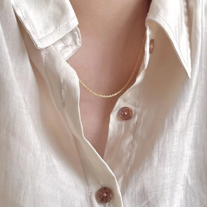 Close-up of minimalist gold 925 sterling silver shell necklace on a white linen shirt