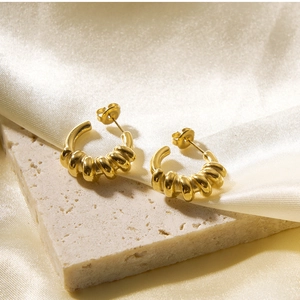Macro shot of 18k gold plated spring coiled hoop earrings on a beige stone surface