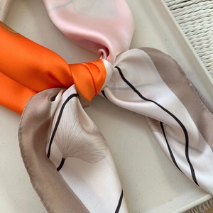 Elegant silk scarf with orange ginkgo leaf pattern tied in a knot on a white tray