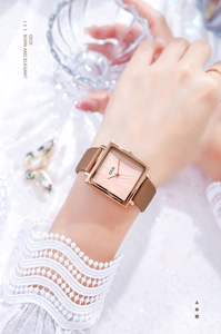 Detail of rose gold square watch with brown leather strap worn by a woman with lace sleeve