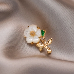Elegant gold flower brooch with white shell petals and a green gemstone drop charm