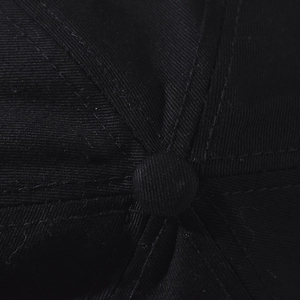 Close-up of cotton twill fabric texture and top crown button on a black baseball cap