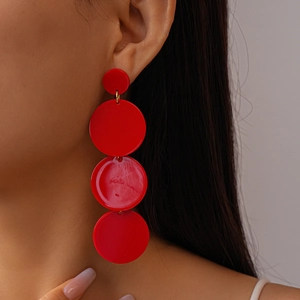 Macro detail of red layered acrylic geometric drop earrings worn by a female model