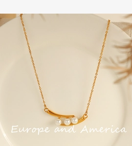 Détail d'un collier doré avec trois perles sur un pendentif dans un plateau blanc