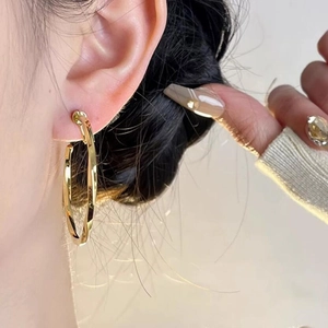 Detail of twisted gold metal hoop earring shown on ear for a minimalist French chic look