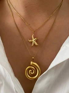 Close-up of layered 18k gold starfish pendant and textured spiral ring necklace on model