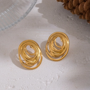 Macro shot of gold spiral geometric earrings with abstract swirl design on textured surface