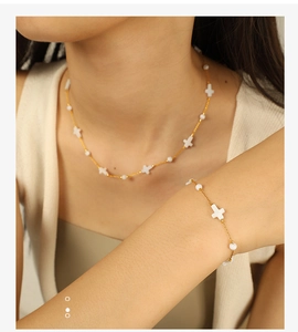 Detail of 18k gold plated titanium necklace and bracelet set with white cross beads on a model