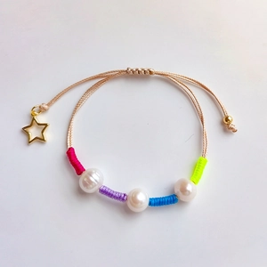 Detail of handmade braided pearl bracelet featuring a hollow gold star charm and colorful silk