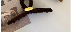Détail d'une pince à cheveux en velours marron avec un emblème ovale en métal doré