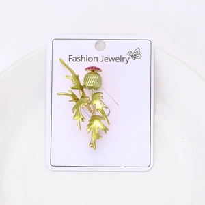Close-up of alloy enamel primrose brooch in green and pink on a white card