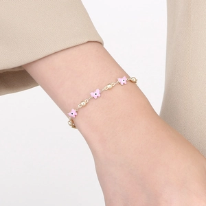Detail of gold chain bracelet with pink enamel butterfly charm on a wrist