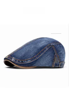 Detail of dark blue washed denim flat cap with orange stitching and side metal buckle