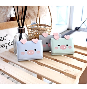 Close-up of cute cartoon pig tri-fold wallets in pastel blue, green, and grey on a wooden rack