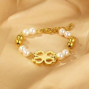 Detail of gold clover pendant on pearl bracelet with adjustable chain over silk fabric
