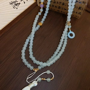 Detail of light blue glass beaded necklace with white tassels and gold accents