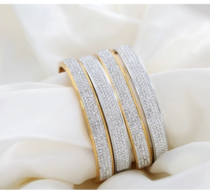 Macro detail of gold and silver plated full-diamond bangles on white silk background