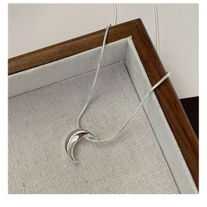 Detailansicht des silbernen Mondanhängers mit Schlangenkette auf einem Leinentablett
