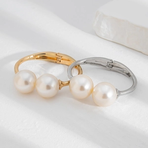Detailed view of layered gold and silver pearl hinge bracelets on a minimalist background