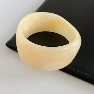 Close-up of wide ivory resin geometric bangle resting on a black leather handbag