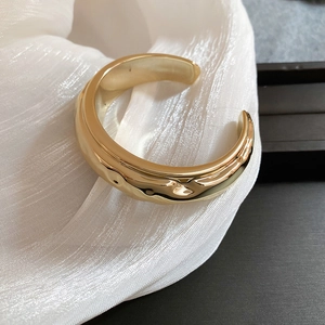 Gros plan d'un bracelet manchette doré à texture irrégulière sur soie blanche