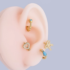 Detail of gold ear cuffs with turquoise heart and bow motifs on a silicone model
