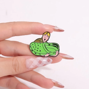 Cartoon-Emaille-Pin einer Figur in einem grünen Clog, gehalten von Fingern