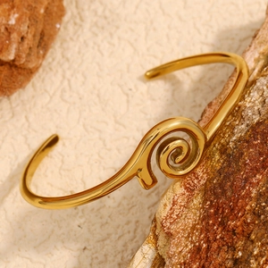Detailed view of an 18K gold plated spiral donut bangle on a natural stone background