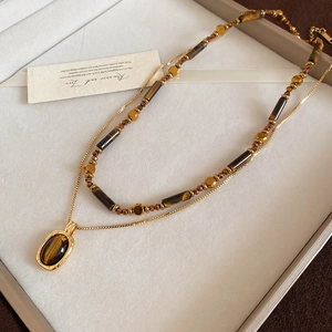 Detail of double-layer necklace with tiger eye beads and golden oval pendant