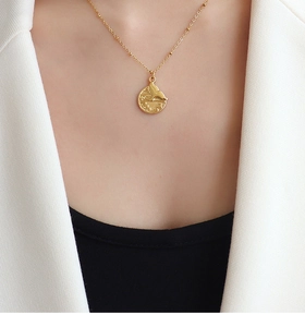 Detail shot of a golden fishtail medallion pendant on a delicate bead chain necklace