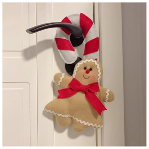 Detail of plush gingerbread man and candy cane felt ornament hanging on a white door