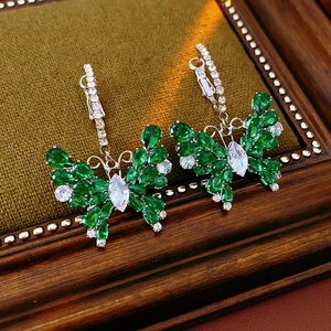 Detail of silver butterfly earrings with green and white zircons on green velvet