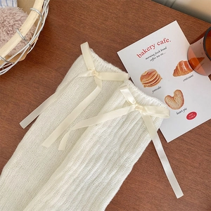 Detailed knit texture of cream leg warmers featuring elegant satin ribbon bow accents