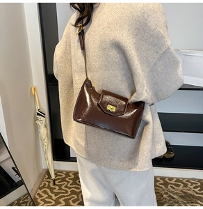 Detail view of dark brown patent leather shoulder bag with gold twist lock on model