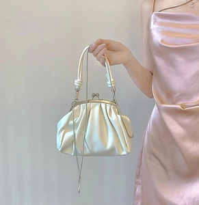 Detail of a creamy white ruched dumpling bag with satin texture and metal clasp closure