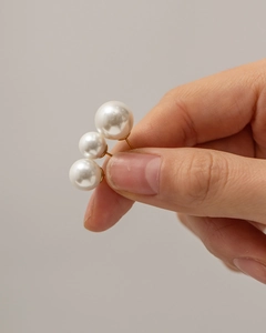 Close-up of three graded sizes of round white pearl earrings with gold pins held by hand