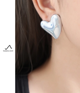 Close-up of polished stainless steel large heart stud earrings worn by a model