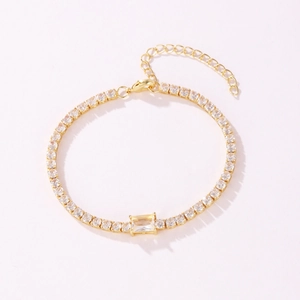 Detailed macro shot of a gold tennis bracelet featuring a central emerald-cut zircon