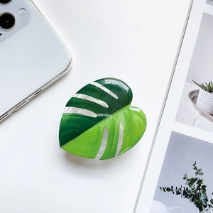 Close-up of Monstera leaf phone grip with green acetic acid finish on a white desk
