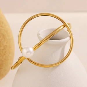 Detail view of a gold knot bracelet with a white pearl on a ceramic vase