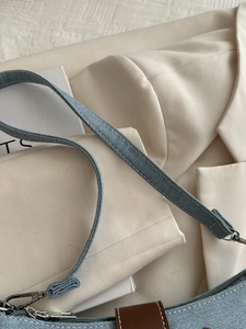Detail of blue denim shoulder bag featuring silver metal hooks and white stitching