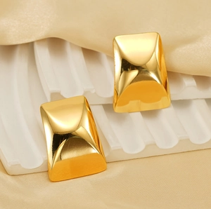 Macro detail of rectangle gold-plated earrings on white texture and satin background