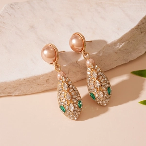 Detail of gold snake-head drop earrings with faux pearls and sparkling green gemstones