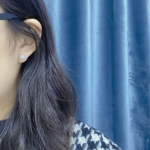 Close-up of minimalist freshwater pearl earrings worn on ear with soft focus background