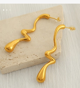 Detail of gold wavy twisted earrings with drop ends on beige stone and white fabric