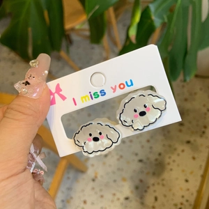 Close-up of cute cream acrylic puppy earrings held by hand against a soft background