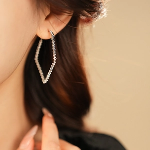 Macro view of silver geometric rhombus earrings with matte texture on model ear
