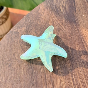 Close-up of iridescent mint green starfish hair claw clip on dark wooden surface