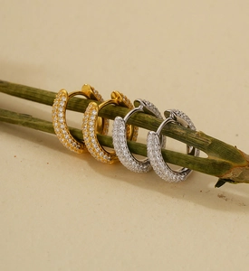 Macro shot of silver and gold U-shape huggie earrings with pave crystals on green stems