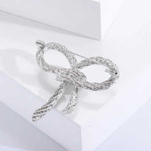 Detailed close-up of a silver bow brooch with woven texture and a safety pin clasp